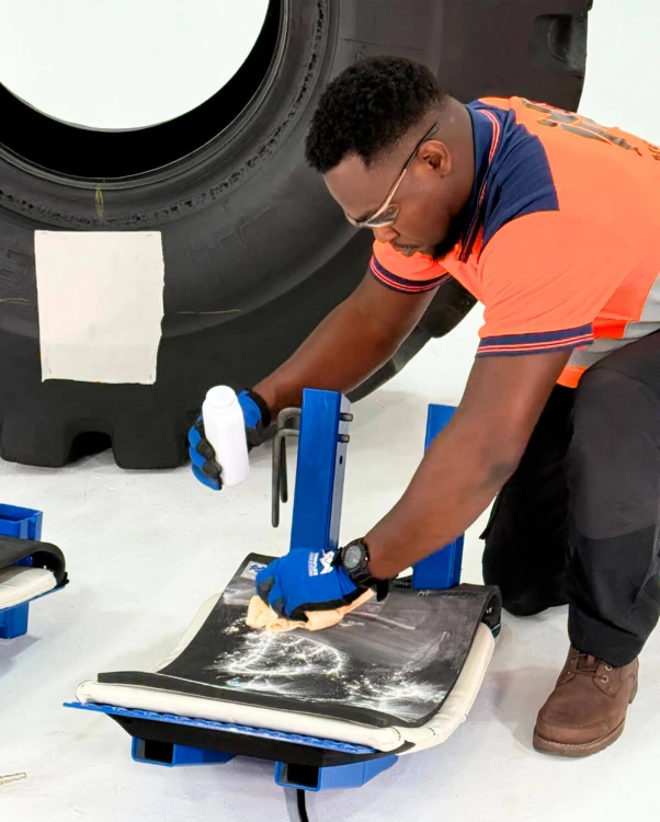 Serwisant w rękawicach ochronnych nakłada talk na elastyczną poduszkę grzewczą systemu Monaflex, przygotowując ją do wulkanizacji opony OTR