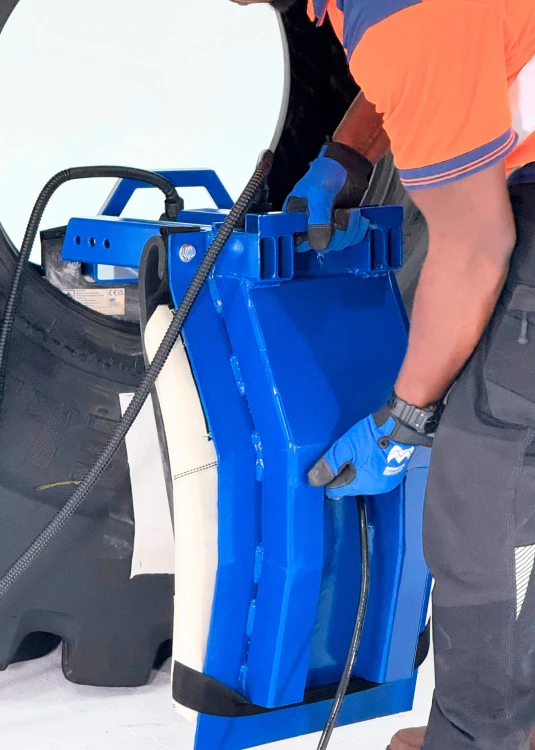 Zbliżenie na dłonie serwisanta montującego niebieską ramę systemu Monaflex do naprawy ścian bocznych opony wielkogabarytowej OTR. Widoczne poduszki dociskowe i przewody