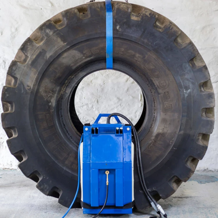 Gotowy do pracy system wulkanizacyjny Monaflex OTR zamontowany na ścianie bocznej dużej opony przemysłowej (bieżnik 26.5 R 25). Urządzenie spięte niebieskim pasem transportowym